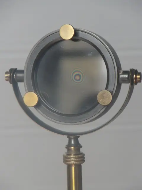 Photograph of a Hooke apparatus showing Newton's rings (iridescent) illuminated in white light.