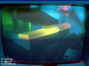 False colour image of an Nd:YAG laser prototype at FNSPE CTU, Prague: Blue channel is all visible radiation. Green colour is the 808 nm NIR diode pumping (200 W pulsed). Red colour is the 1060 nm NIR laser output. (Note the scattered red at upper right from the laser optics.) The active medium in the center is a highly-doped (ca. 3 %) Nd:YAG crystal with grazing incidence of the beam. The pumping beam comes to the middle of the front surface and is absorbed within few mm under the surface.